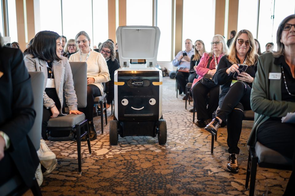 A small delivery robot with a smiling face in the aisle of a conference room.