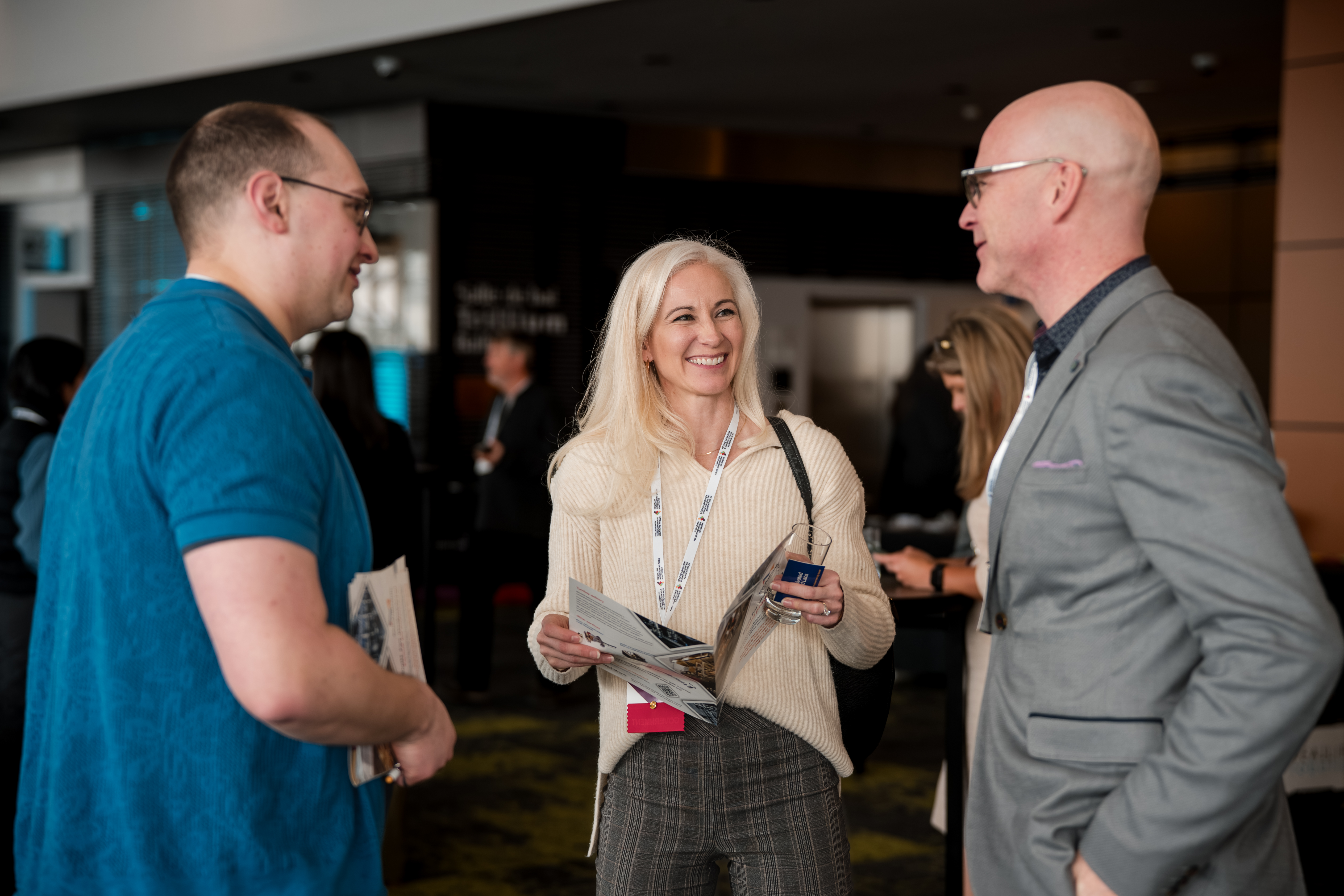 Three professionals smiling and conversing animatedly at an indoor networking event.