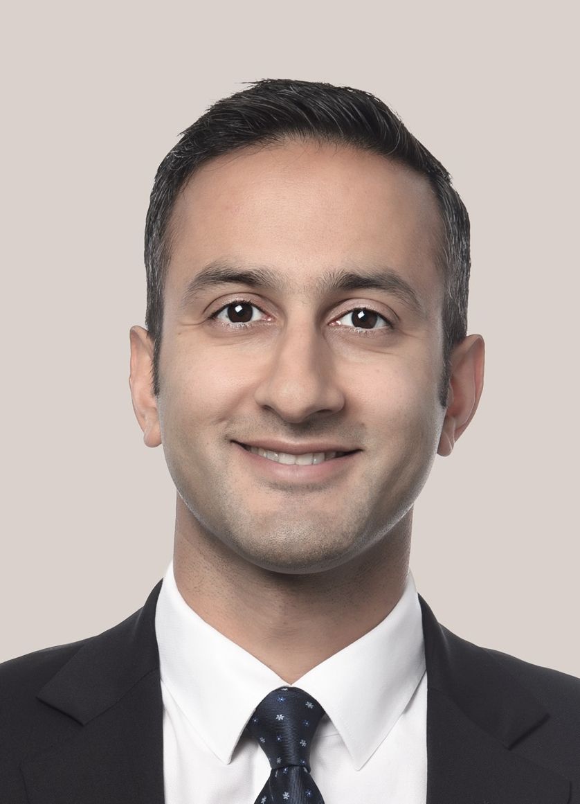 Smiling man in a dark suit and patterned tie, headshot against a plain background.