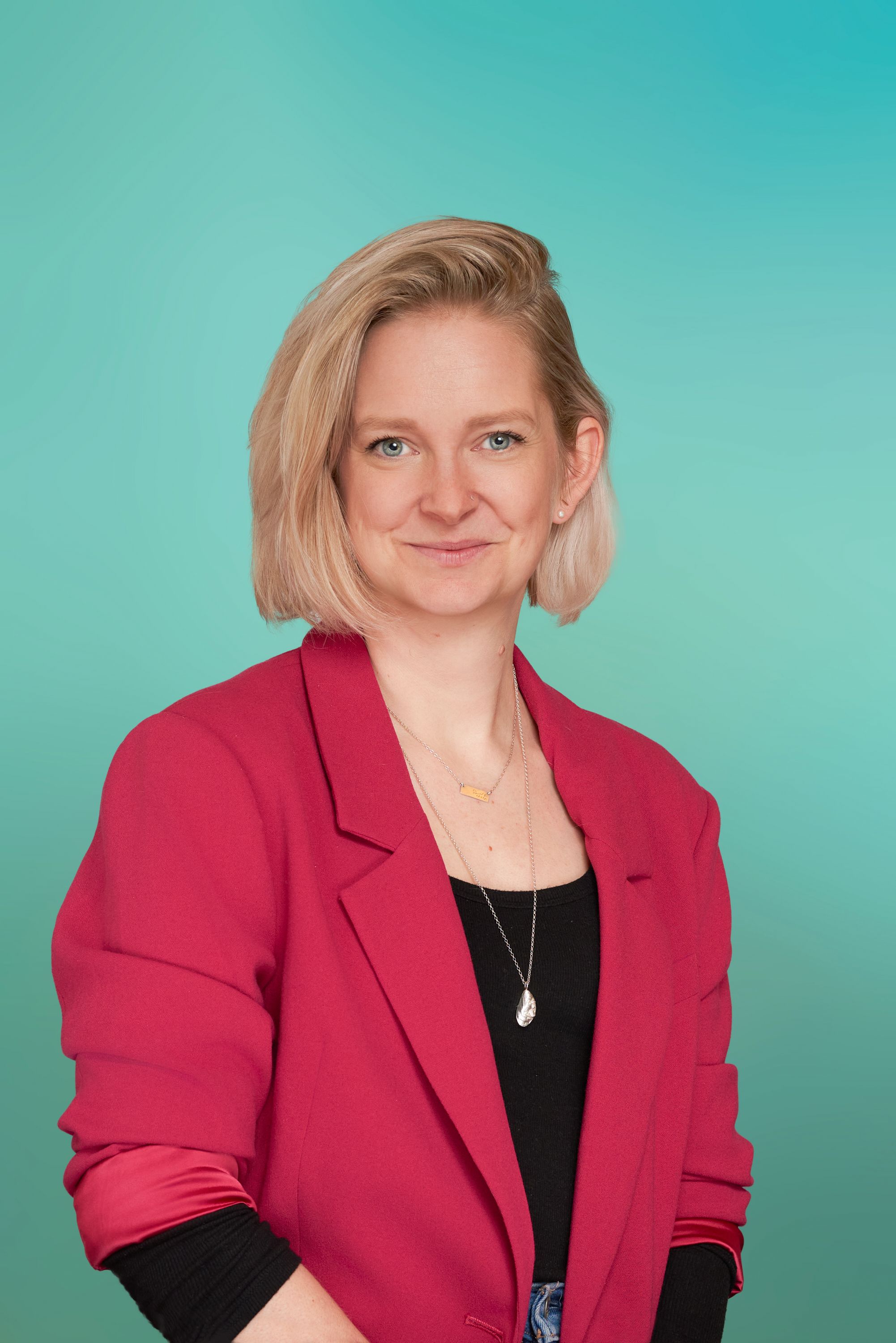 Blonde woman in a bright pink blazer smiling subtly against a teal background.