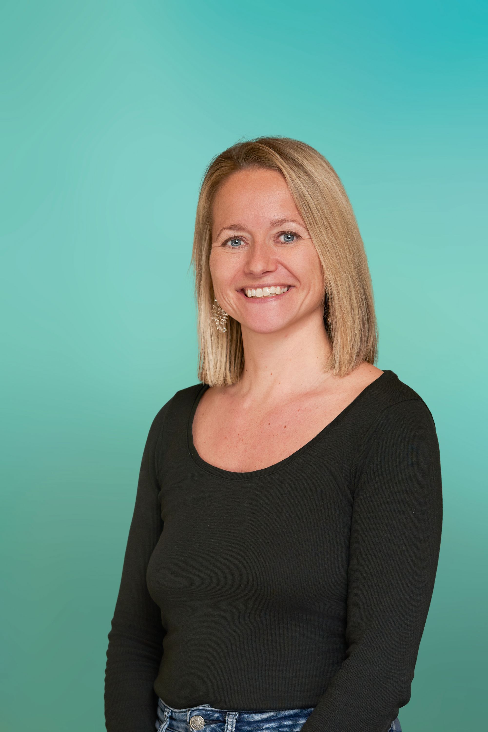 Friendly blonde woman in a black shirt smiling brightly against a teal background.
