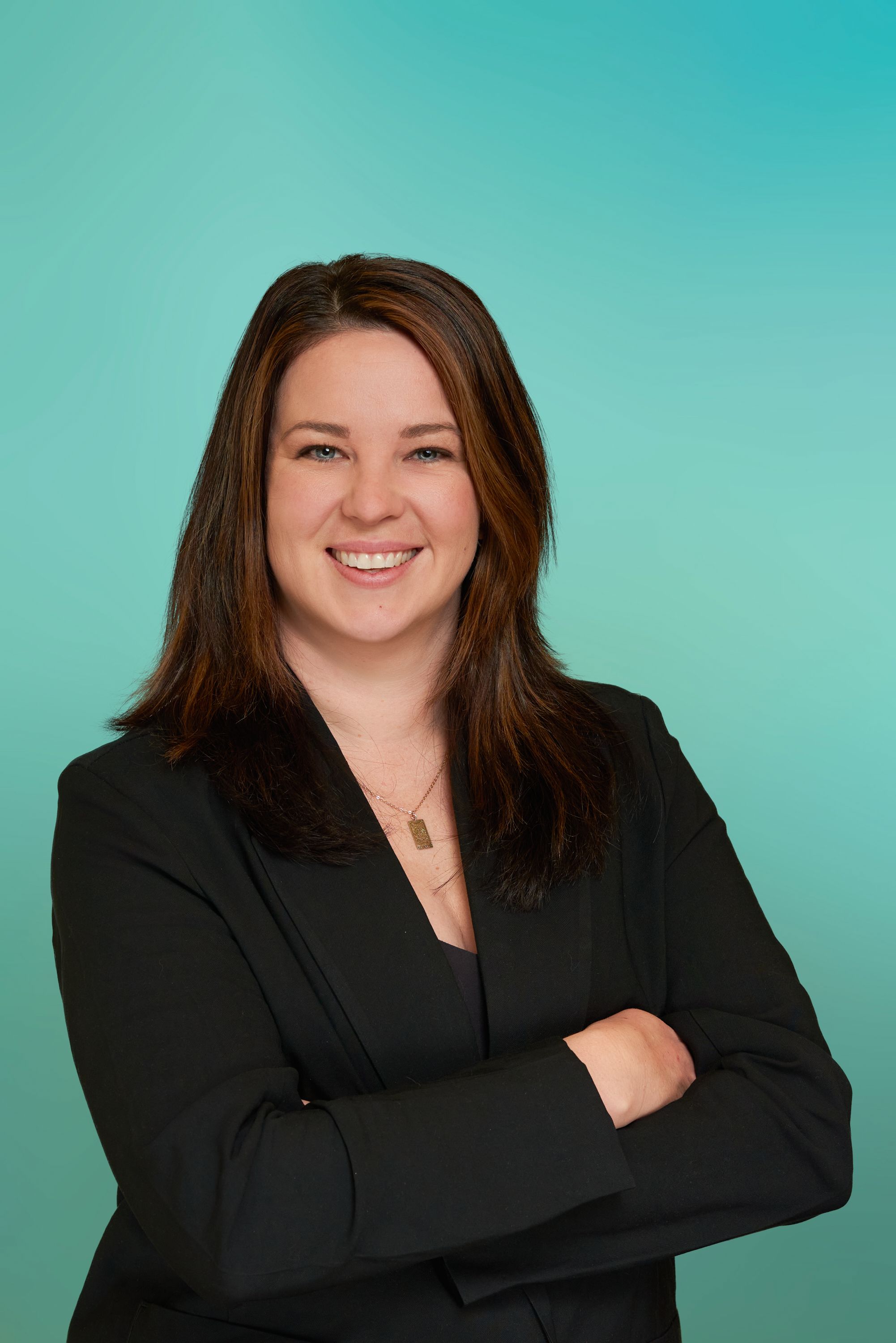 Smiling professional woman with long brown hair wearing a black blazer, arms crossed.