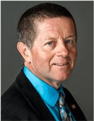 Professional headshot of a man with short hair wearing a blue shirt and black jacket.