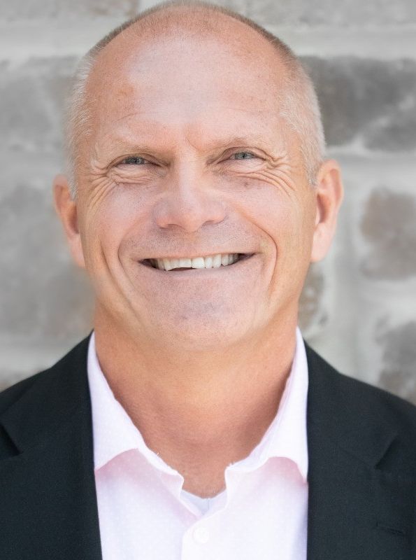 Smiling bald man in a dark suit jacket, looking directly at the camera.