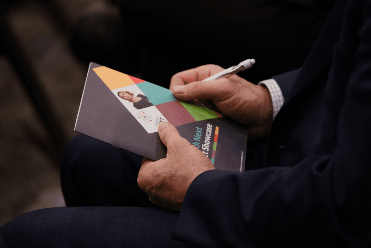 A person in a suit jacket writes notes on a colorful brochure with a pen.