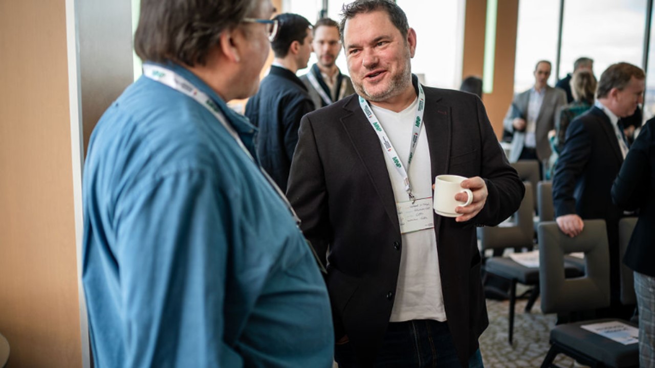 Two men networking at a professional event, one smiling and holding a mug.