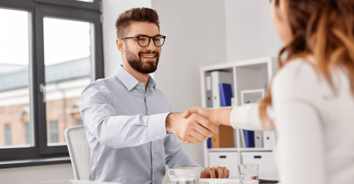 Man and woman shaking hands across a desk in a professional office setting.
