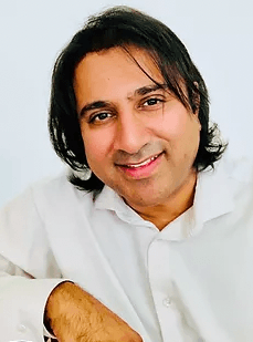 A smiling man with dark hair in a white shirt looks directly at the camera.