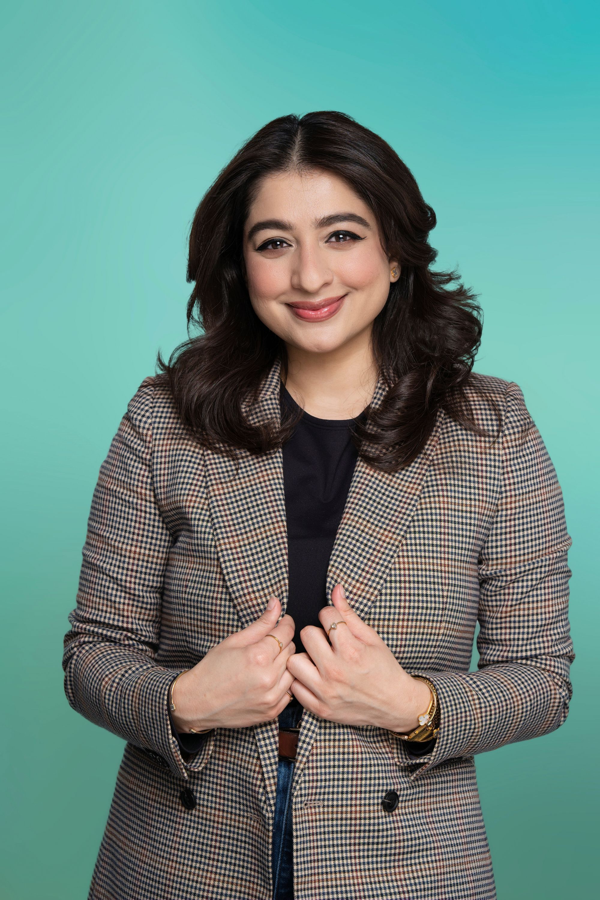 Smiling woman with dark hair in a plaid blazer against a green-blue background.