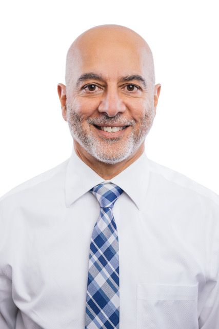 Bald man with a beard smiling, wearing a white shirt and blue checkered tie.
