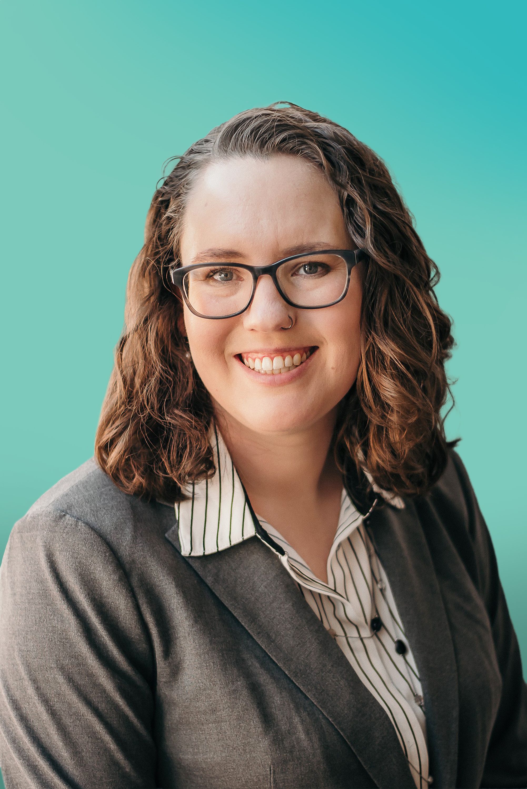 Smiling woman with dark curly hair and glasses wearing a professional blazer.