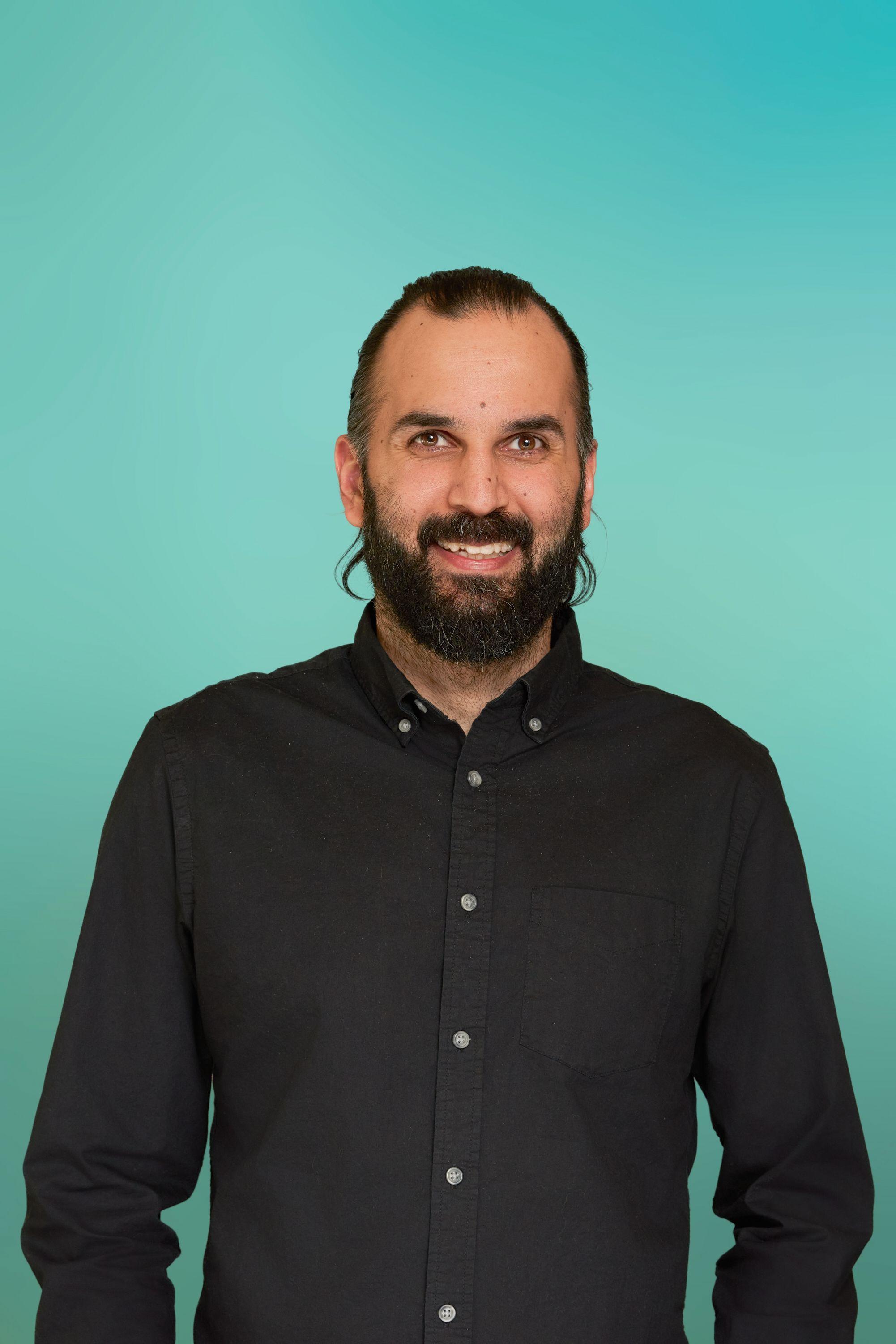 Smiling man with a beard and dark shirt against a blue background.