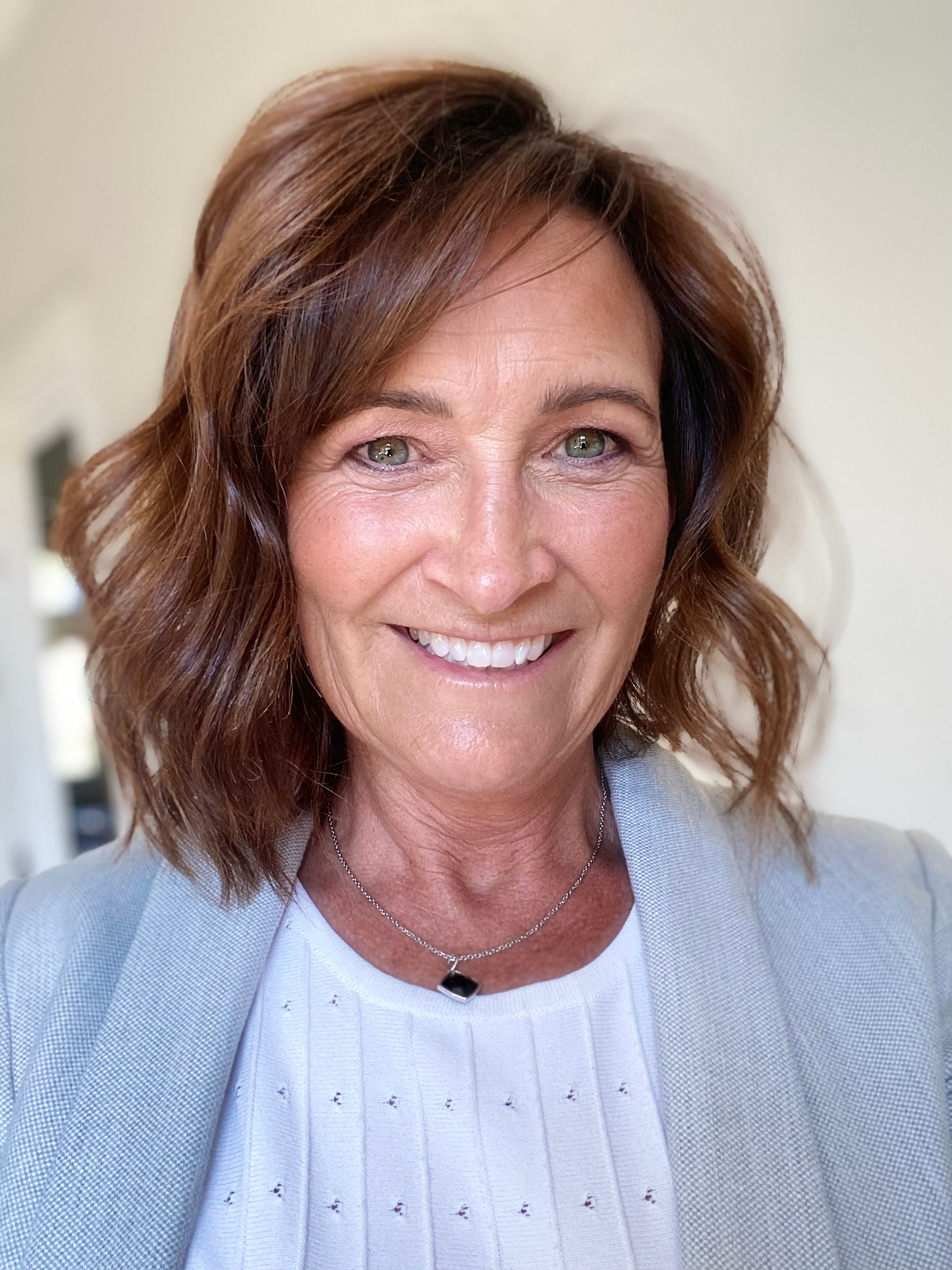 Smiling woman with shoulder-length brown hair wearing a light blue blazer.