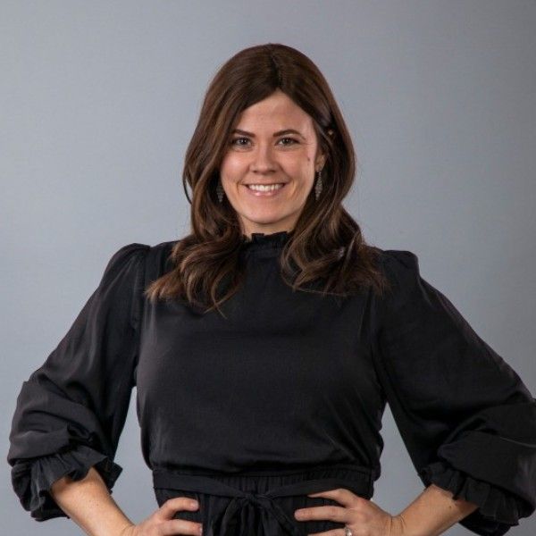 Woman with long dark hair and a black blouse smiling against a gray background.