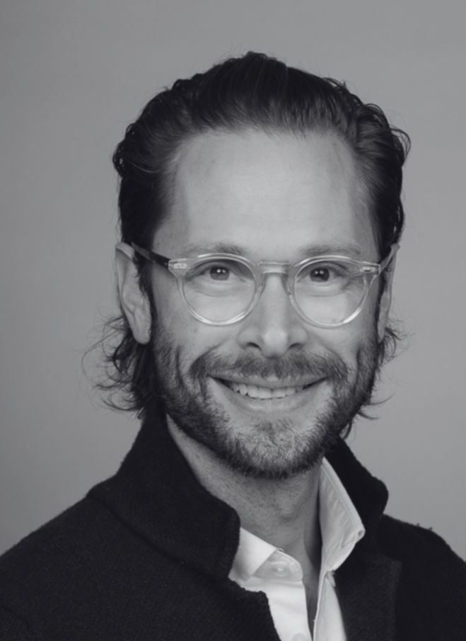 Black and white portrait of a smiling man with glasses, beard, and dark hair.
