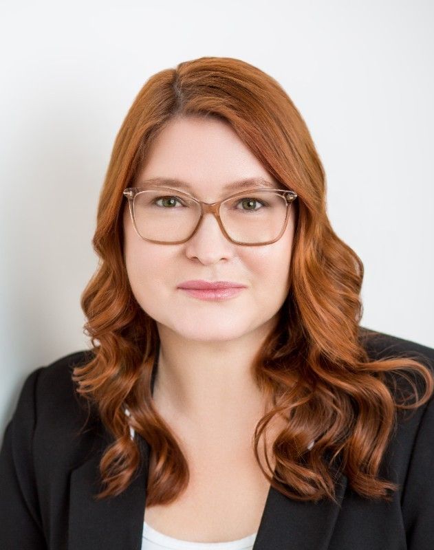 Professional headshot of a woman with red hair and eyeglasses.