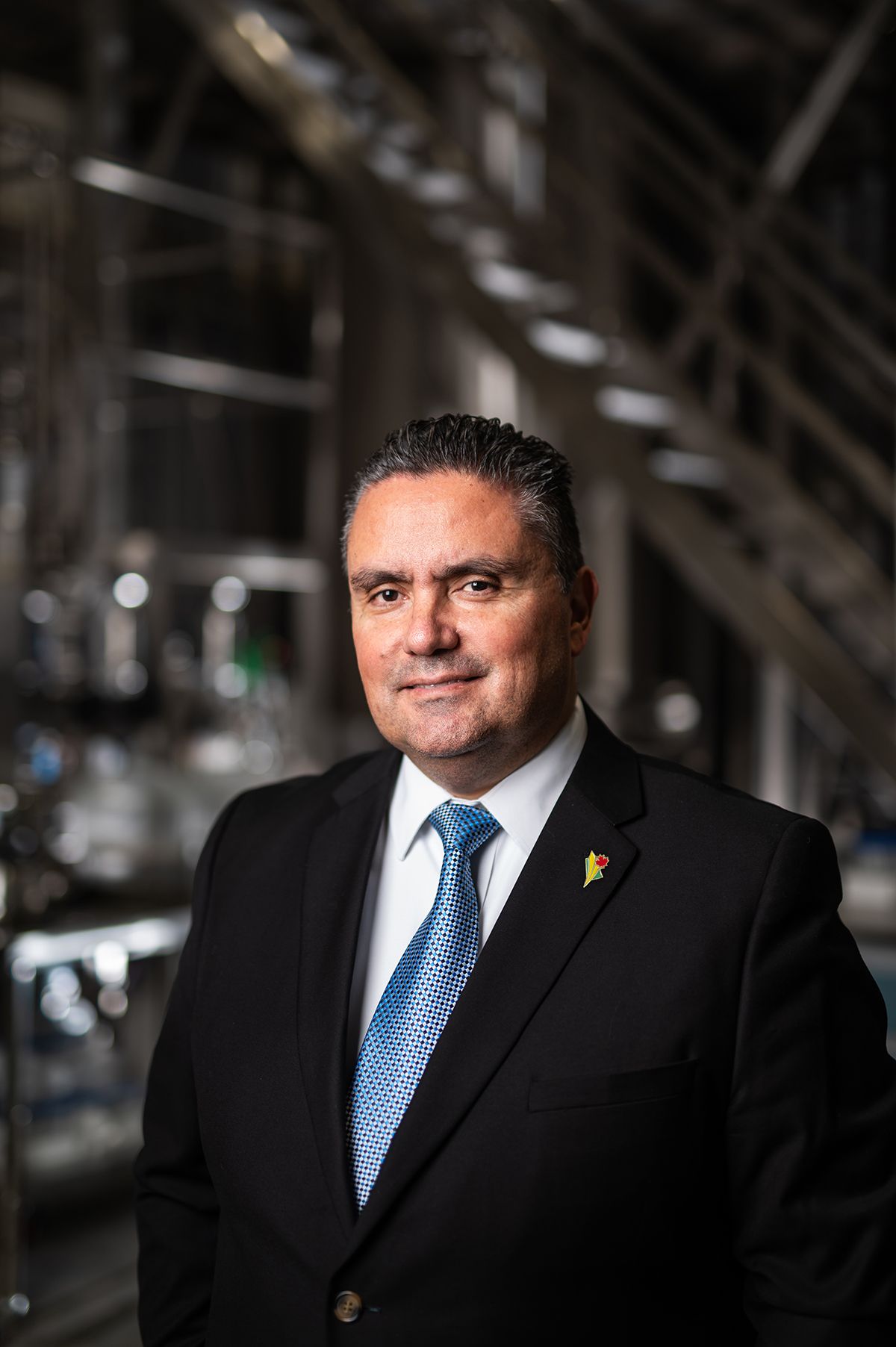 Professional man in dark suit and blue tie smiling in an industrial setting.