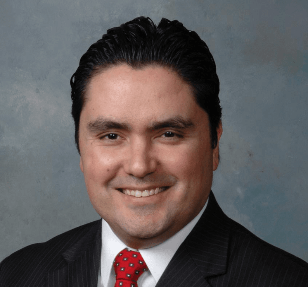 Professional headshot of a smiling man in a dark suit and red tie.