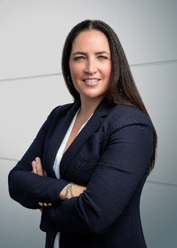 Professional woman with long dark hair, wearing a navy blazer, smiling with arms crossed.