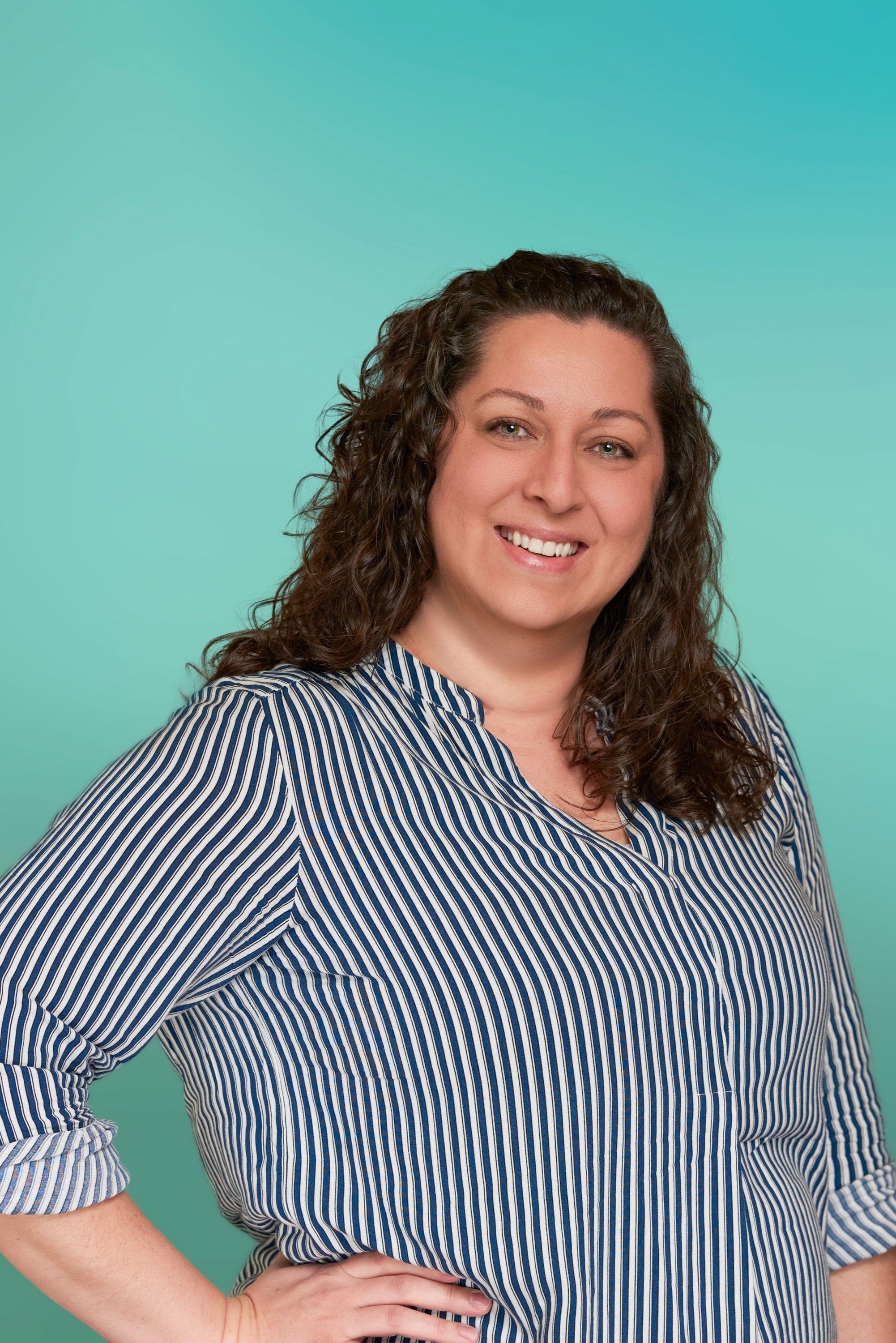 Smiling woman with long curly brown hair and striped shirt against teal background.