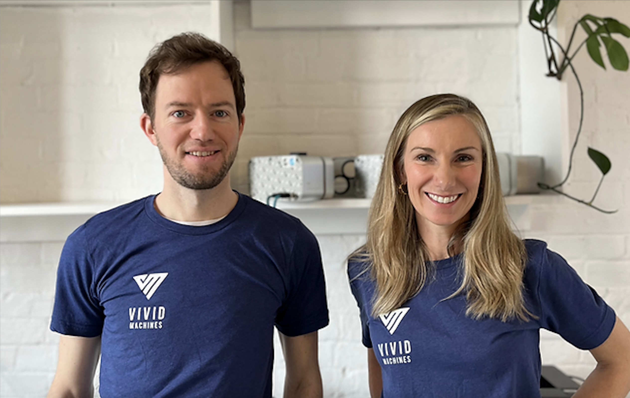 Two smiling people, a man and a woman, wear blue Vivid Instruments t-shirts.