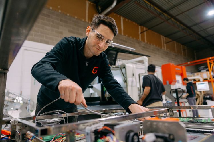 Man in safety glasses diligently working on electronic components in a workshop.