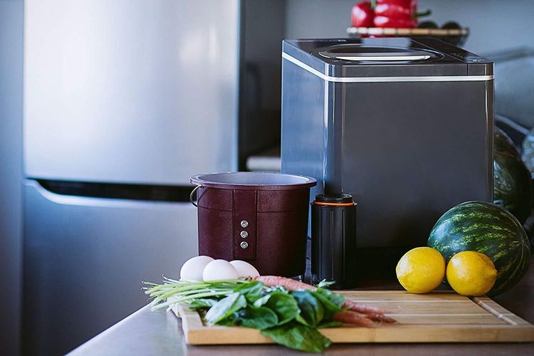 A sleek black kitchen composter sits on a counter with fresh vegetables and fruit.