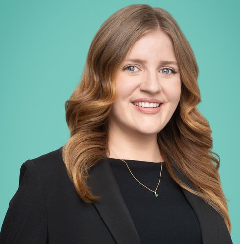 Professional headshot of a smiling woman with long brown hair in a black blazer.