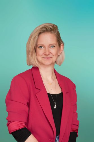 Blonde woman in a bright pink blazer smiling subtly against a teal background.