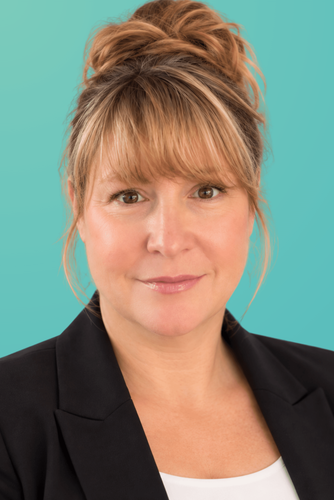Smiling woman with light brown hair in bun, wearing black blazer against teal background.