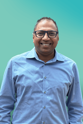 A smiling man in glasses and a blue shirt looks directly at the camera.