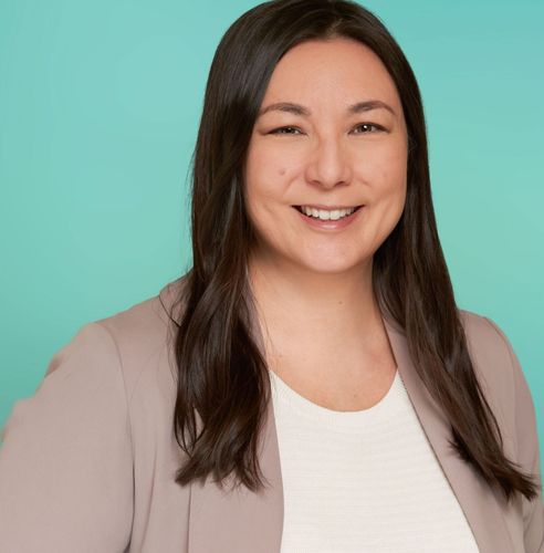 Smiling woman with long dark hair wearing a blazer against a teal background.