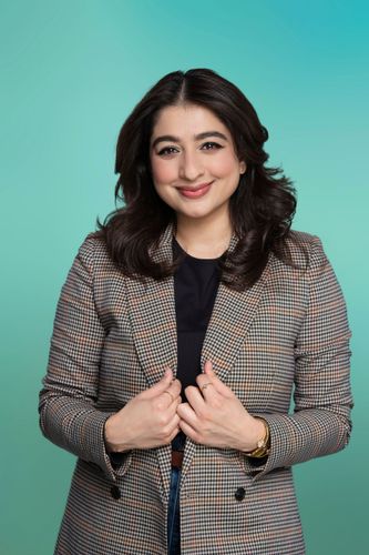 Smiling woman with dark hair in a plaid blazer against a green-blue background.
