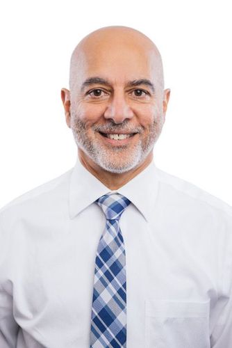 Bald man with a beard smiling, wearing a white shirt and blue checkered tie.