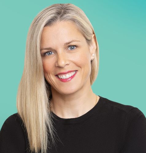 Smiling blonde woman with long hair wearing a black top against a blue-green background.
