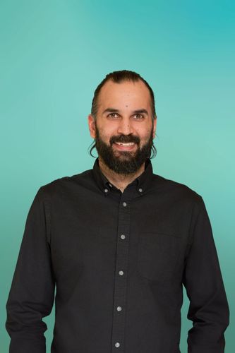 Smiling man with a beard and dark shirt against a blue background.