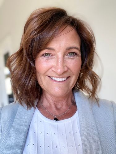 Smiling woman with shoulder-length brown hair wearing a light blue blazer.