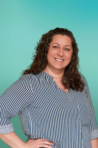 Smiling woman with long curly brown hair and striped shirt against teal background.