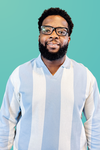 Smiling Black man with glasses and beard wearing a striped shirt.